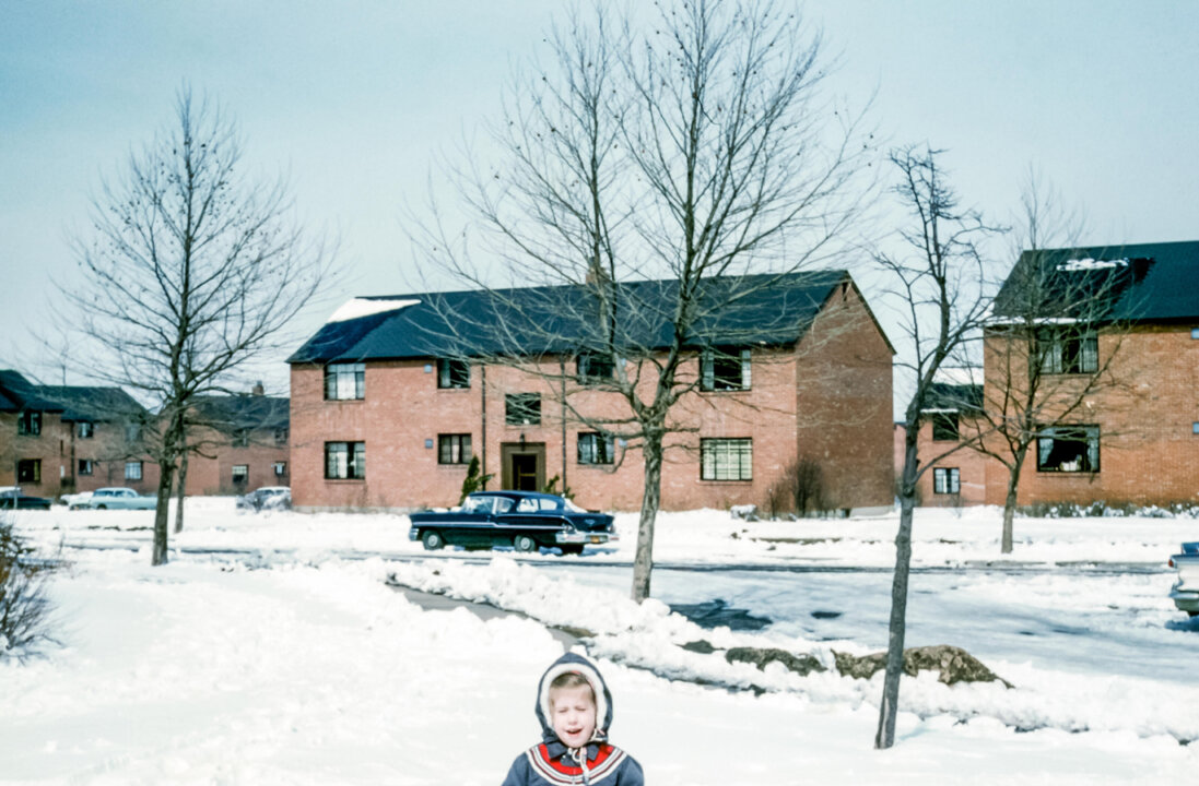 Young girl wearing a Winter coat in a housing estate in Buffalo, New York, USA in the 1950s with American cars on snow covered streets.